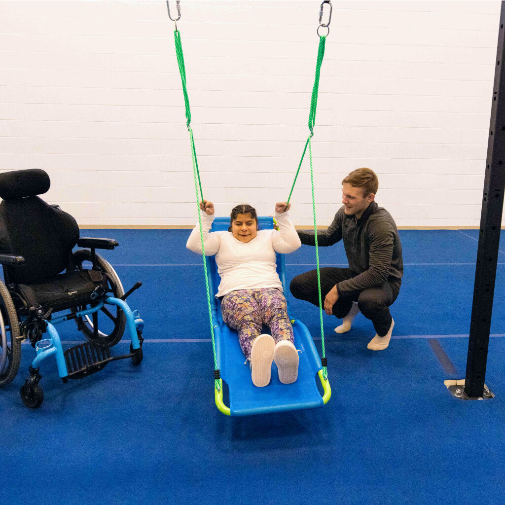 A woman sitting in a lounge chair swing next to her wheelchair with an Occupational Therapist