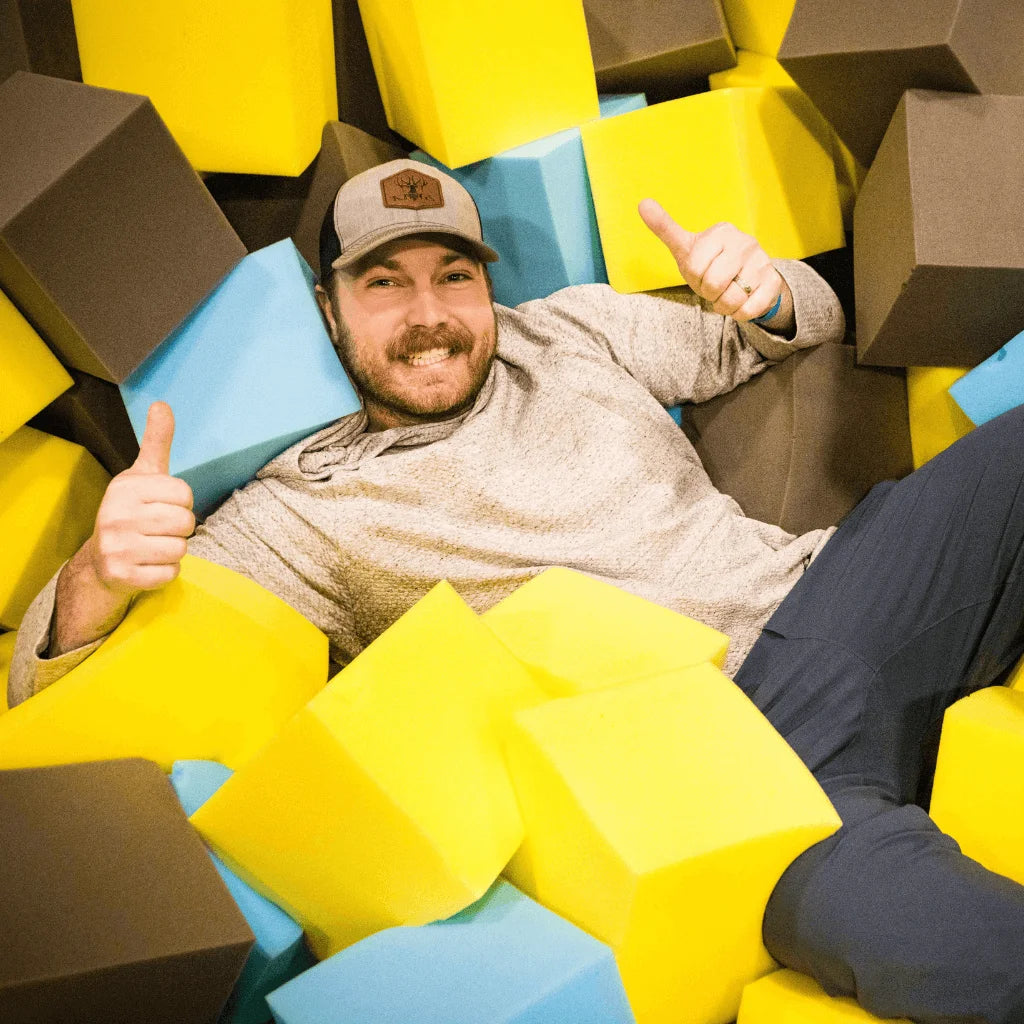 A man smiling and giving a thumbs up while lying in a foam pit