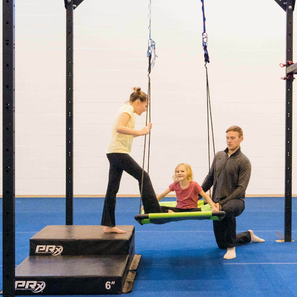 A girl using stackable plyo boxes to climb safely onto a sensory swing