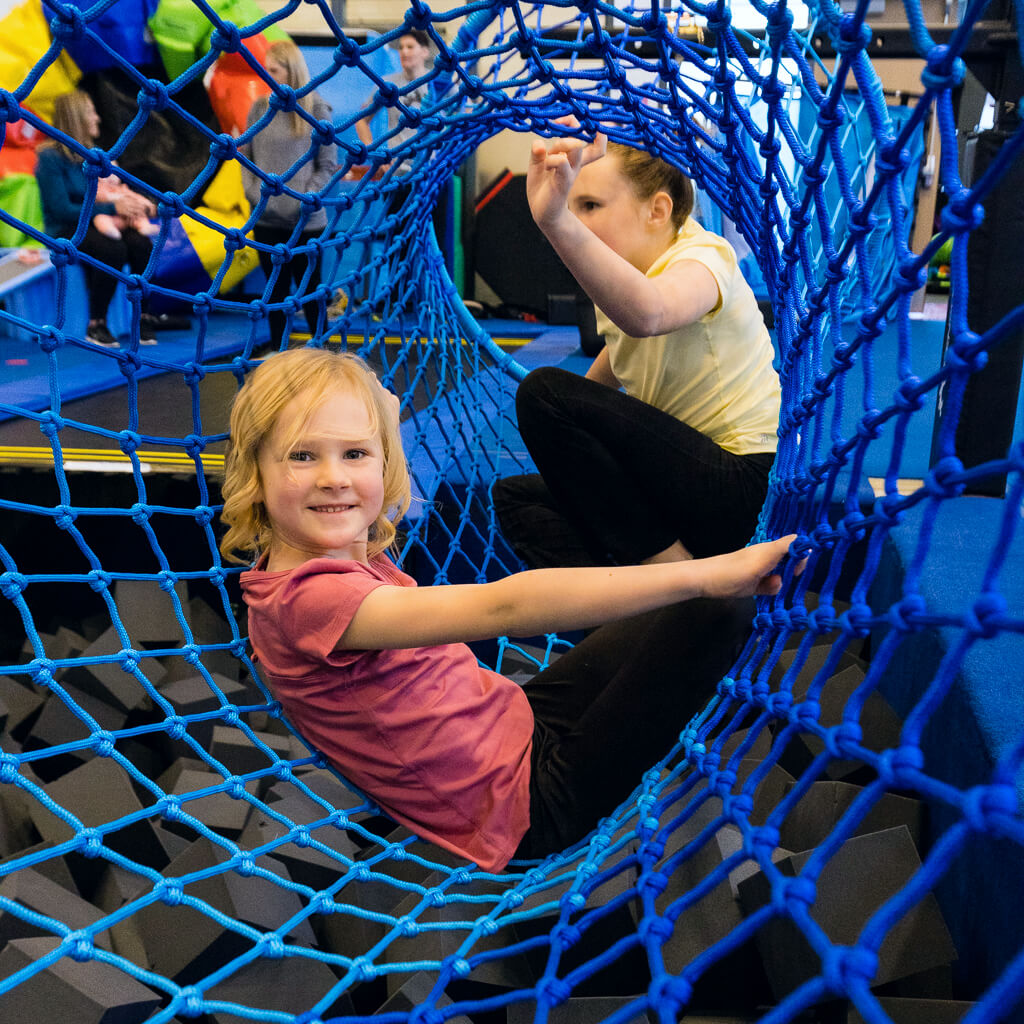 A girl smiling while playing in the rope tunnel