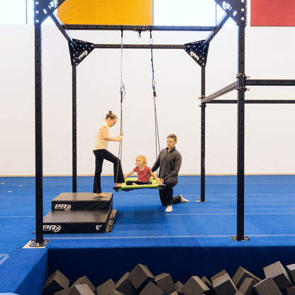 Two girls climbing into a platform sensory swing with the help of an Occupational Therapist