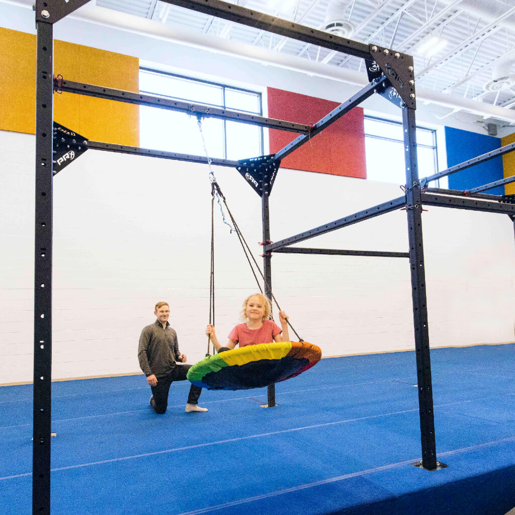 A girl spinning on a sensory saucer swing in a sensory gym