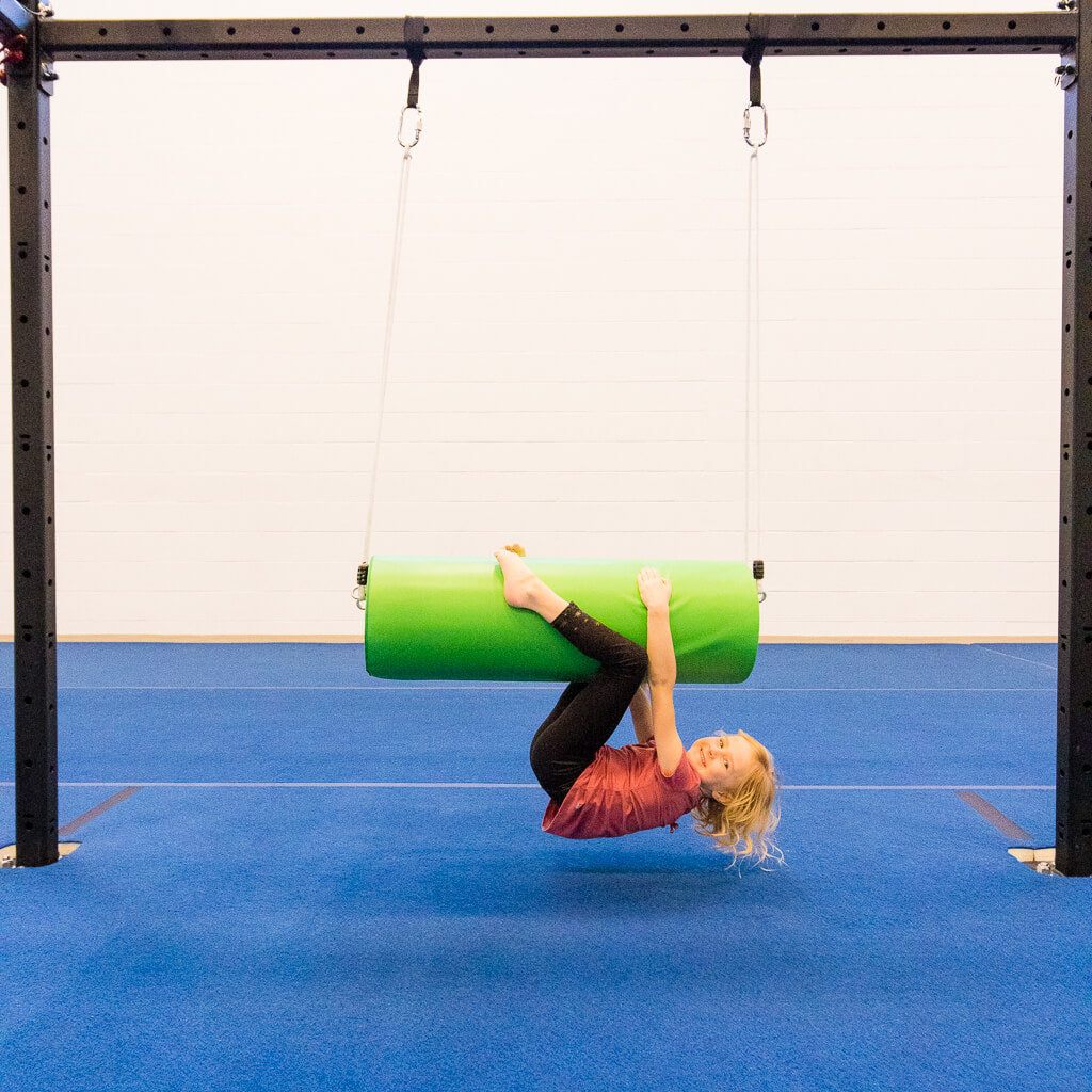 A girl hanging upside down on a round green bolster swing